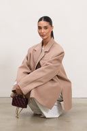 Woman wearing a beige coat holding a purple handbag against a plain background