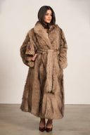 Woman wearing a long brown fur coat against a white background
